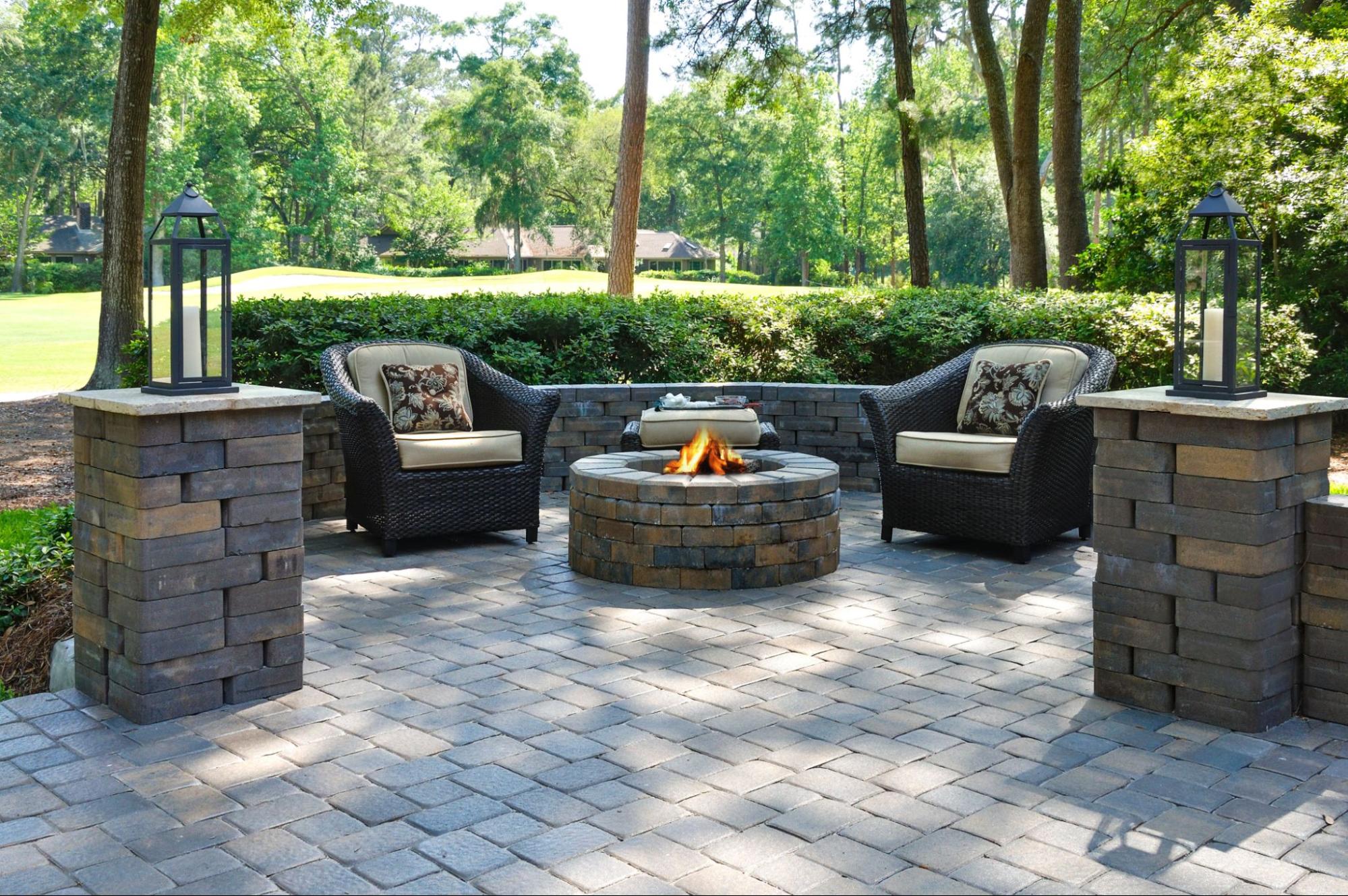 Round stone fire pit with wicker seating and stacked stone columns on paver patio in Cicero, IL by Luxterra Outdoors